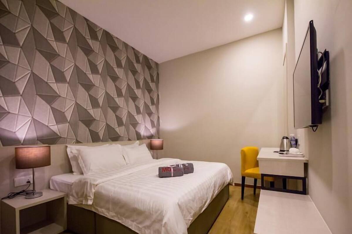 A hotel room with a bed, bedside tables, a desk, a chair, and a geometric-patterned wall.
