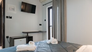 Habitación de hotel con cama, escritorio, televisión y ventana con cortinas.