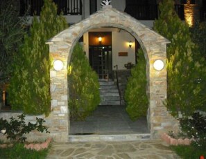 A stone archway leading to a building entrance, surrounded by greenery. - Ballas Hotel (Volos)