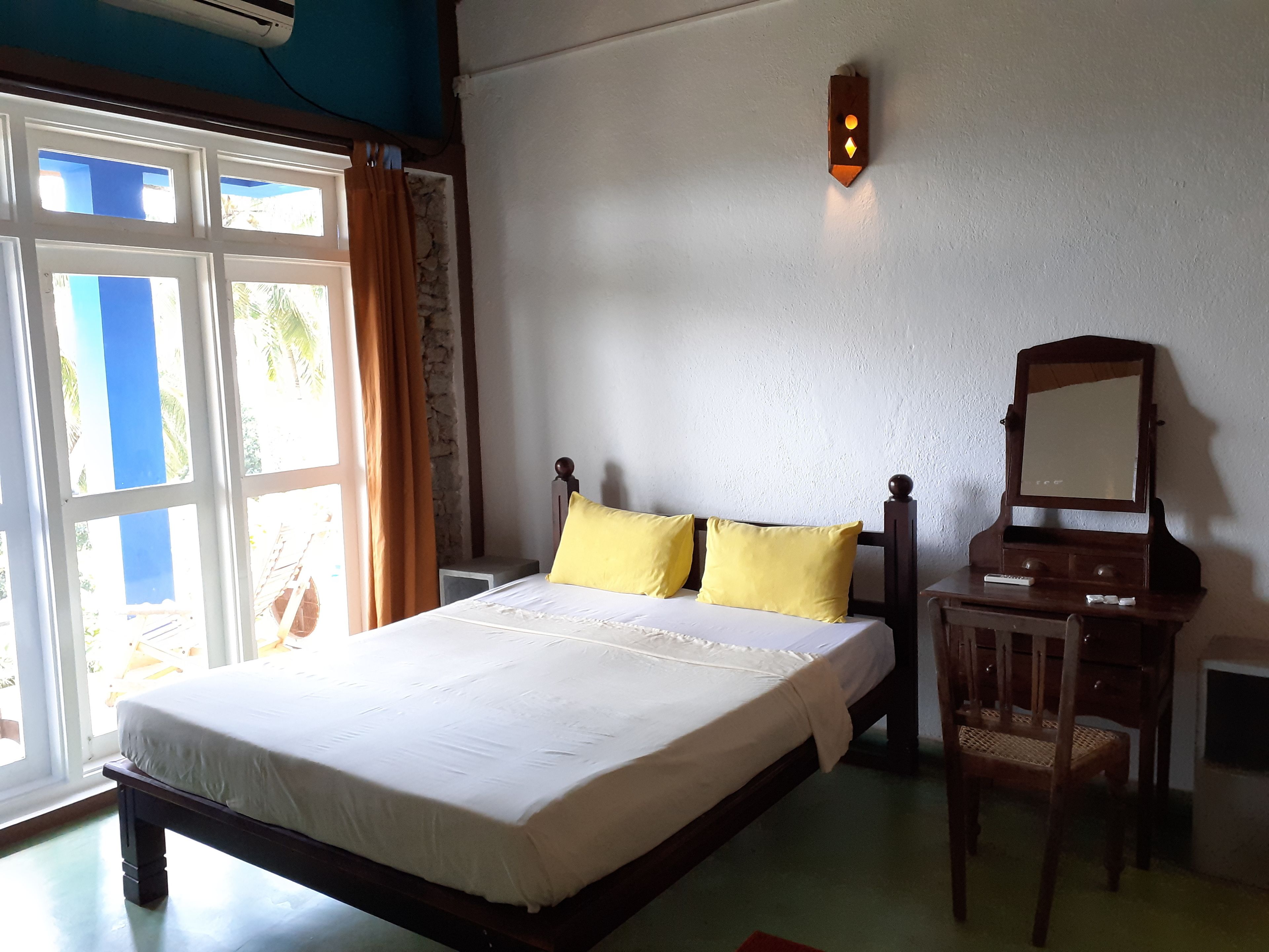 A bedroom with a bed, a wooden nightstand, a chair, a mirror, and a wall-mounted light fixture.