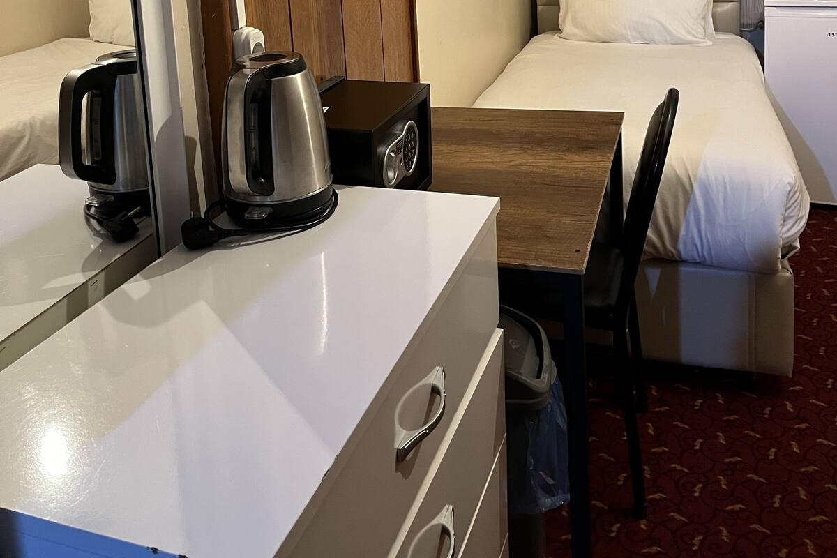 A hotel room with a bed, a desk with a coffee maker, a chair, a wardrobe, and a window with curtains.