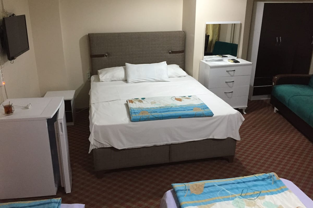 A hotel room with a bed, a desk with a chair, a wardrobe, and a television mounted on the wall.