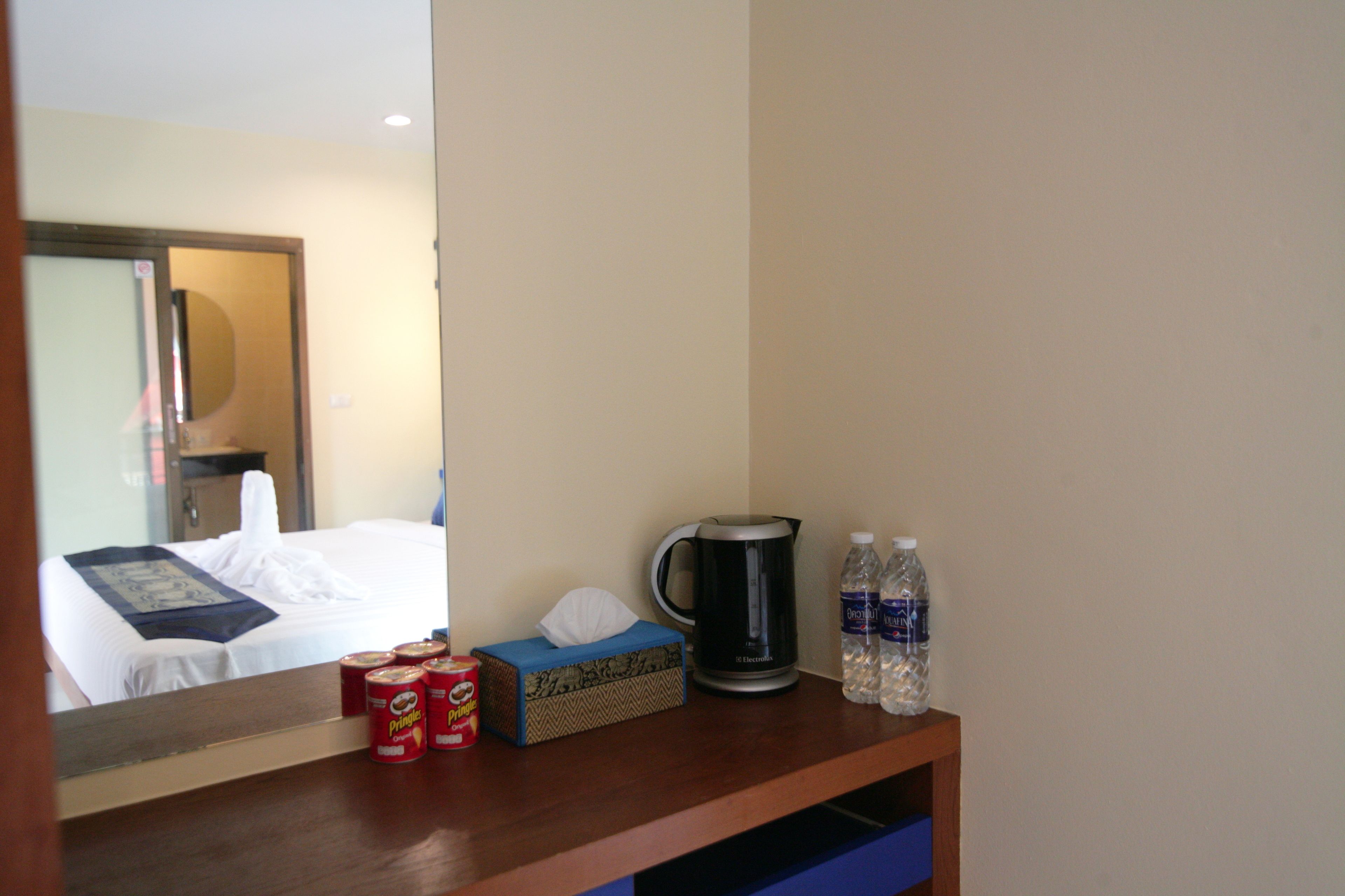 A hotel room with a bed, a bedside table with a tissue box, a kettle, and two bottles of water.