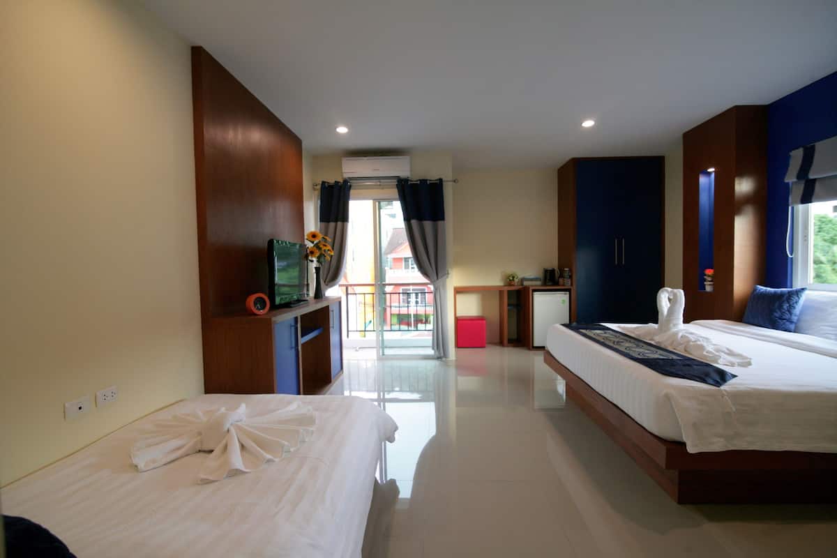A hotel room with two beds, a desk, a small kitchenette, and a view of the outside.