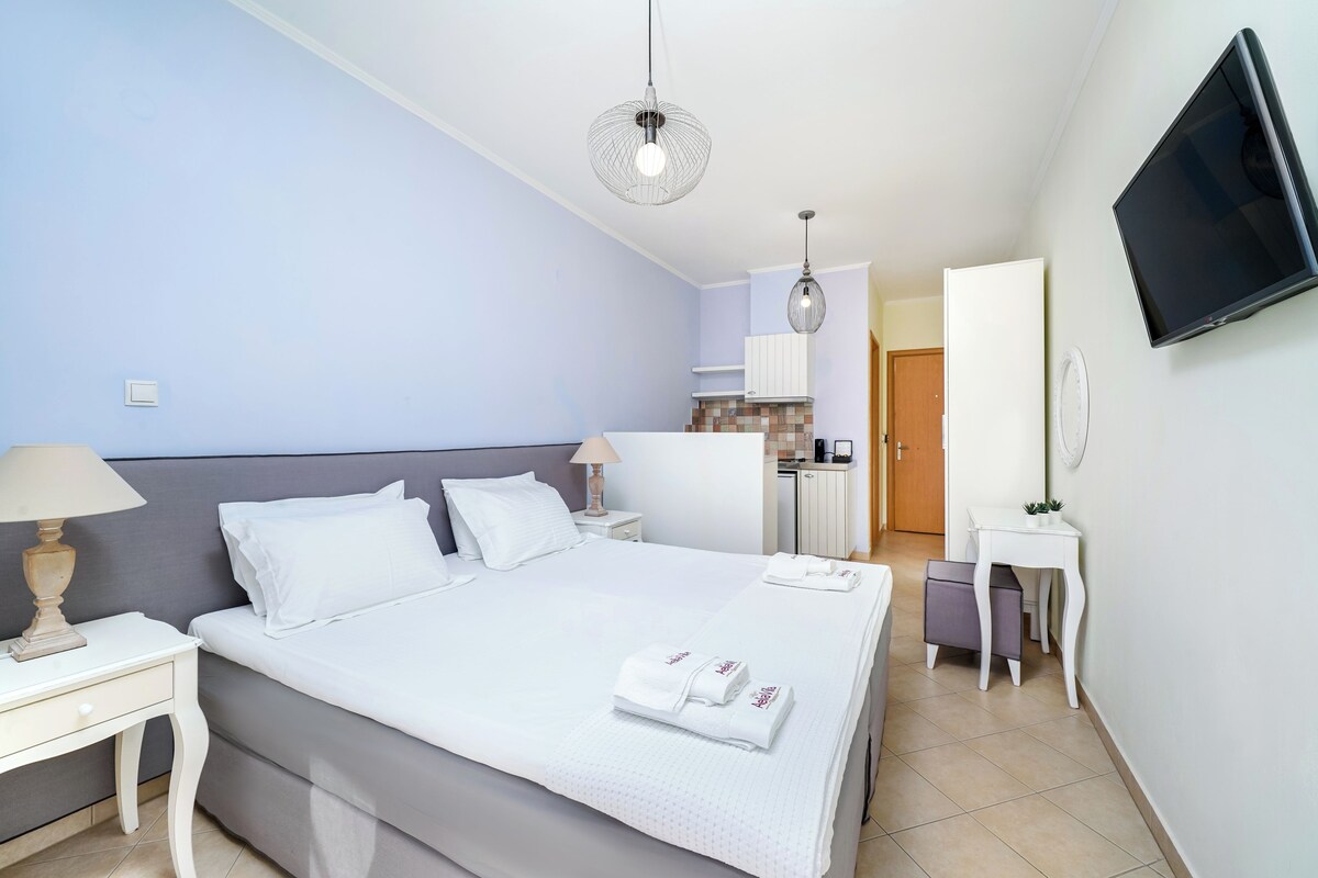 A hotel room with a bed, bedside tables, a TV, and a kitchenette.