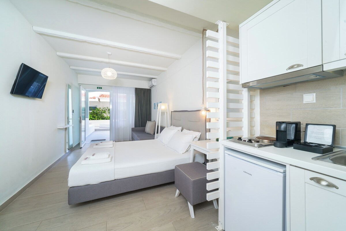 A hotel room with a bed, a desk, a kitchenette, and a television.