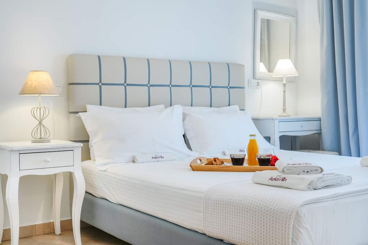 A neatly made bed with white linens, a tray with breakfast items, and a bedside table with a lamp.