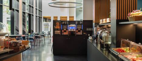 A modern cafe with a self-service coffee machine, a buffet counter with various food items, and a seating area with tables and chairs.
