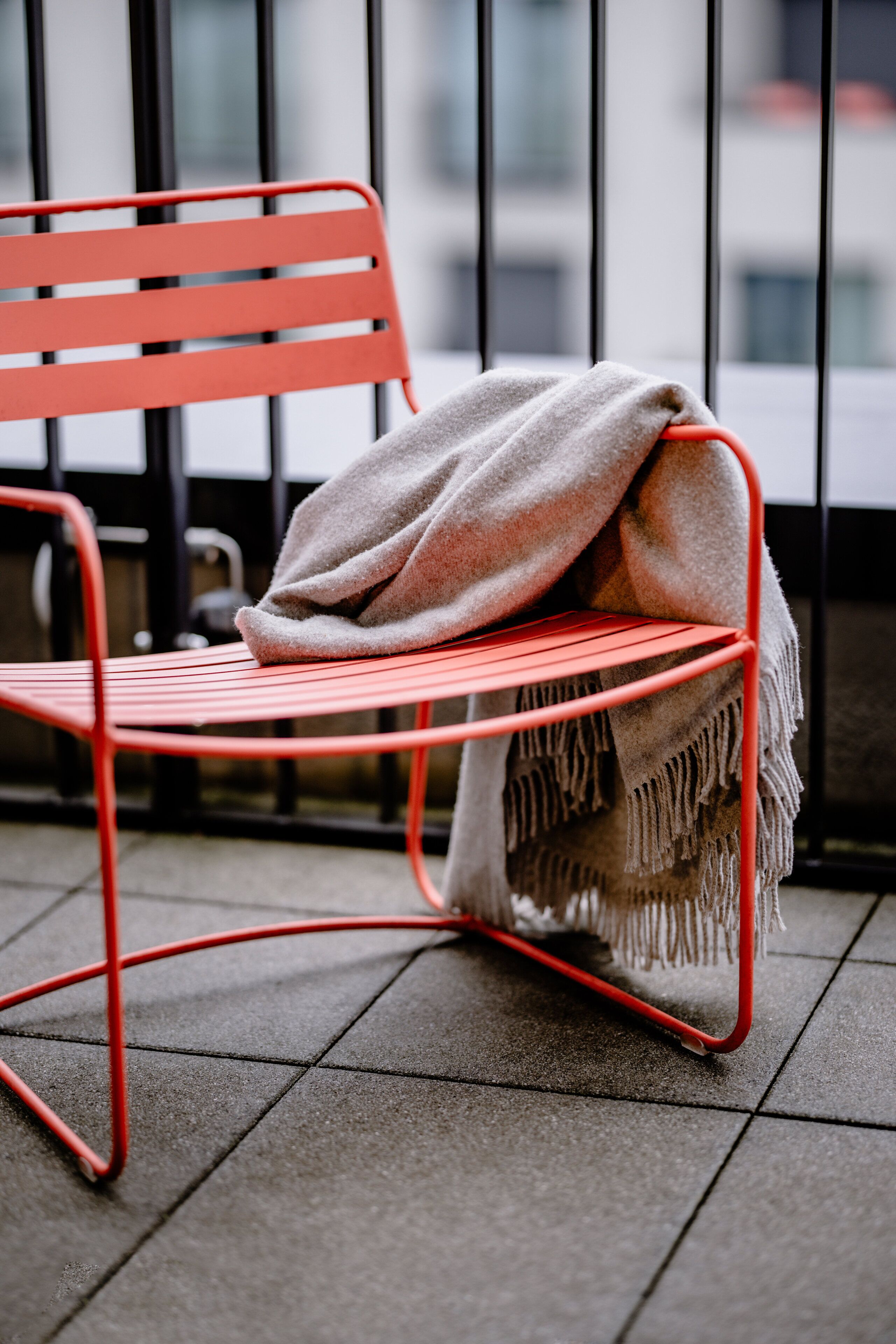A red metal chair with a beige blanket on a tiled balcony.