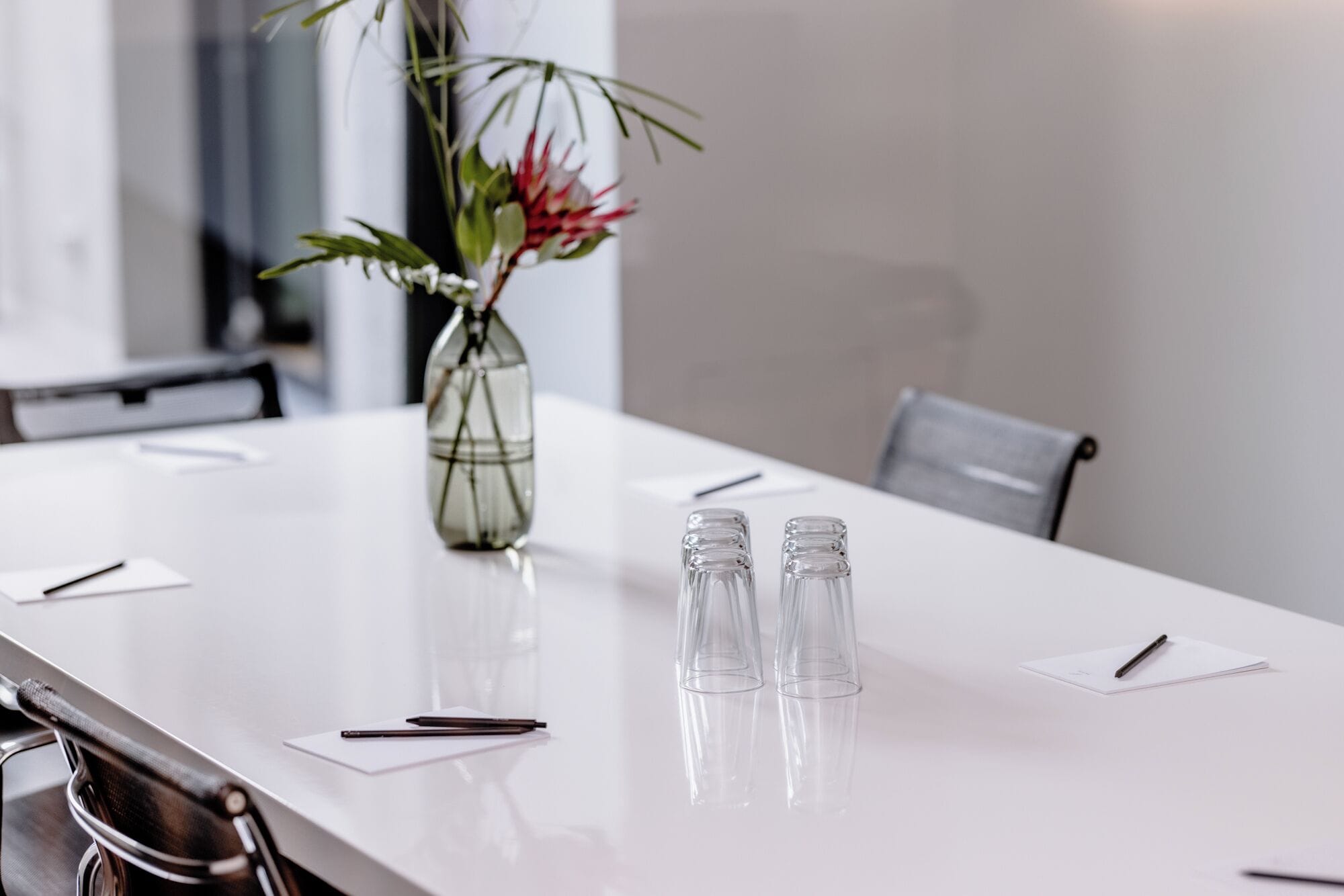 Uma mesa de conferência com um vaso de flores, saleiro e pimenteiro, e canetas em blocos de notas.