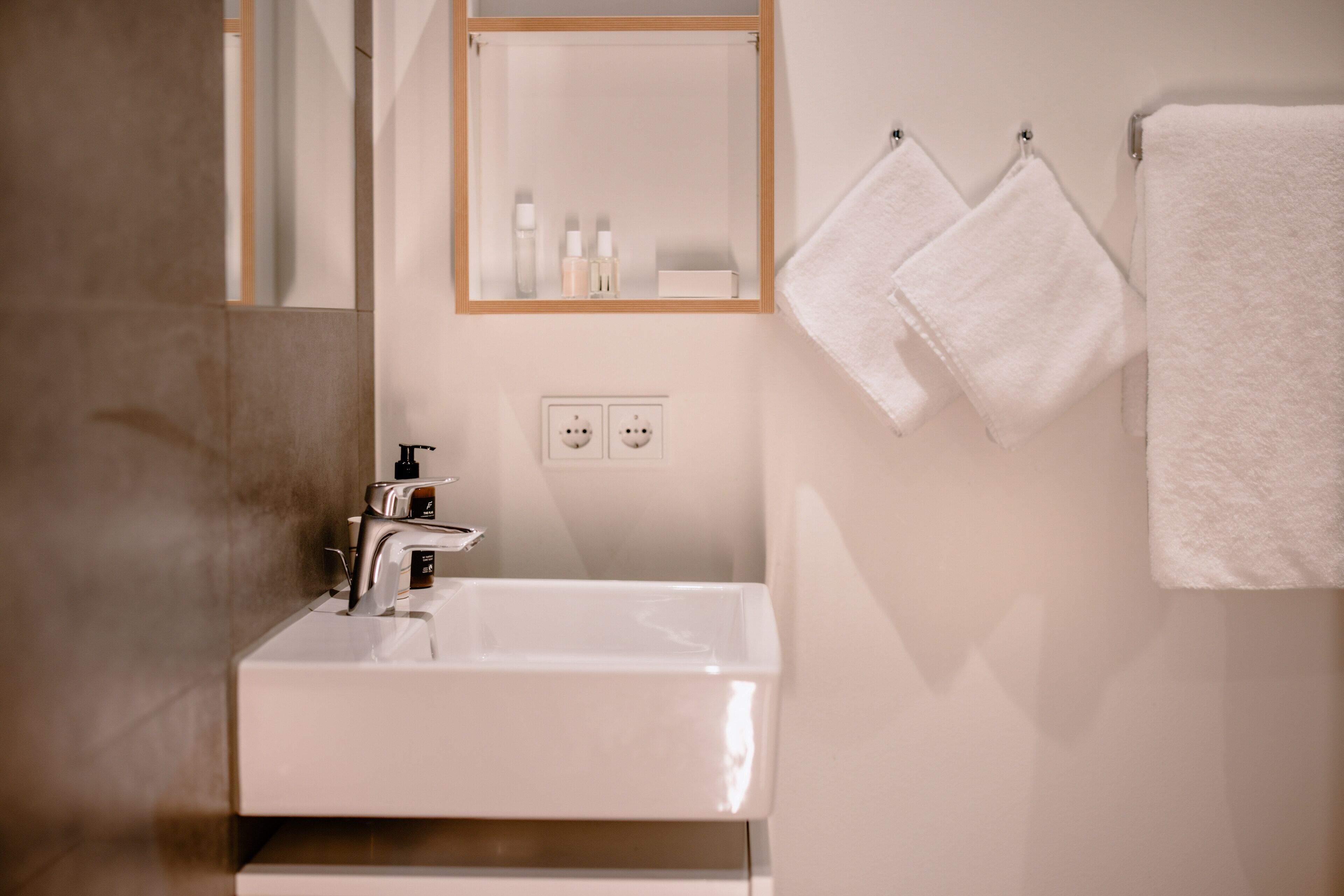 Un baño con un lavamanos blanco, un espejo y dos toallas colgadas en un perchero.