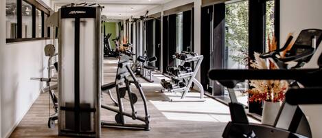 Un gimnasio moderno con diverso equipo de ejercicio, amplias ventanas y suelo de madera.