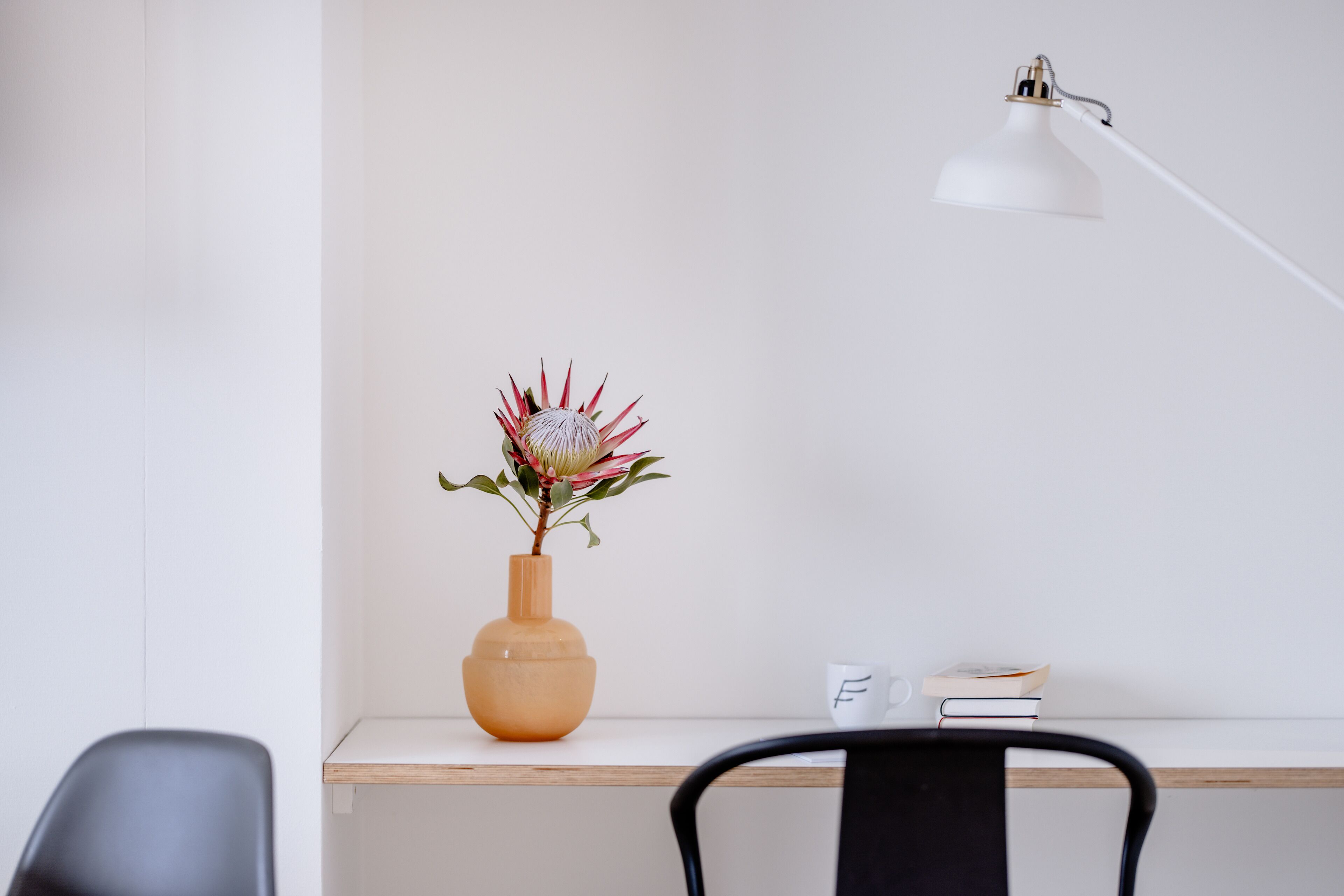A desk with a vase of flowers, a lamp, and a chair.