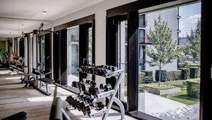 A modern gym with exercise equipment and large windows overlooking a landscaped area. - THE FLAG München M. (Munich)