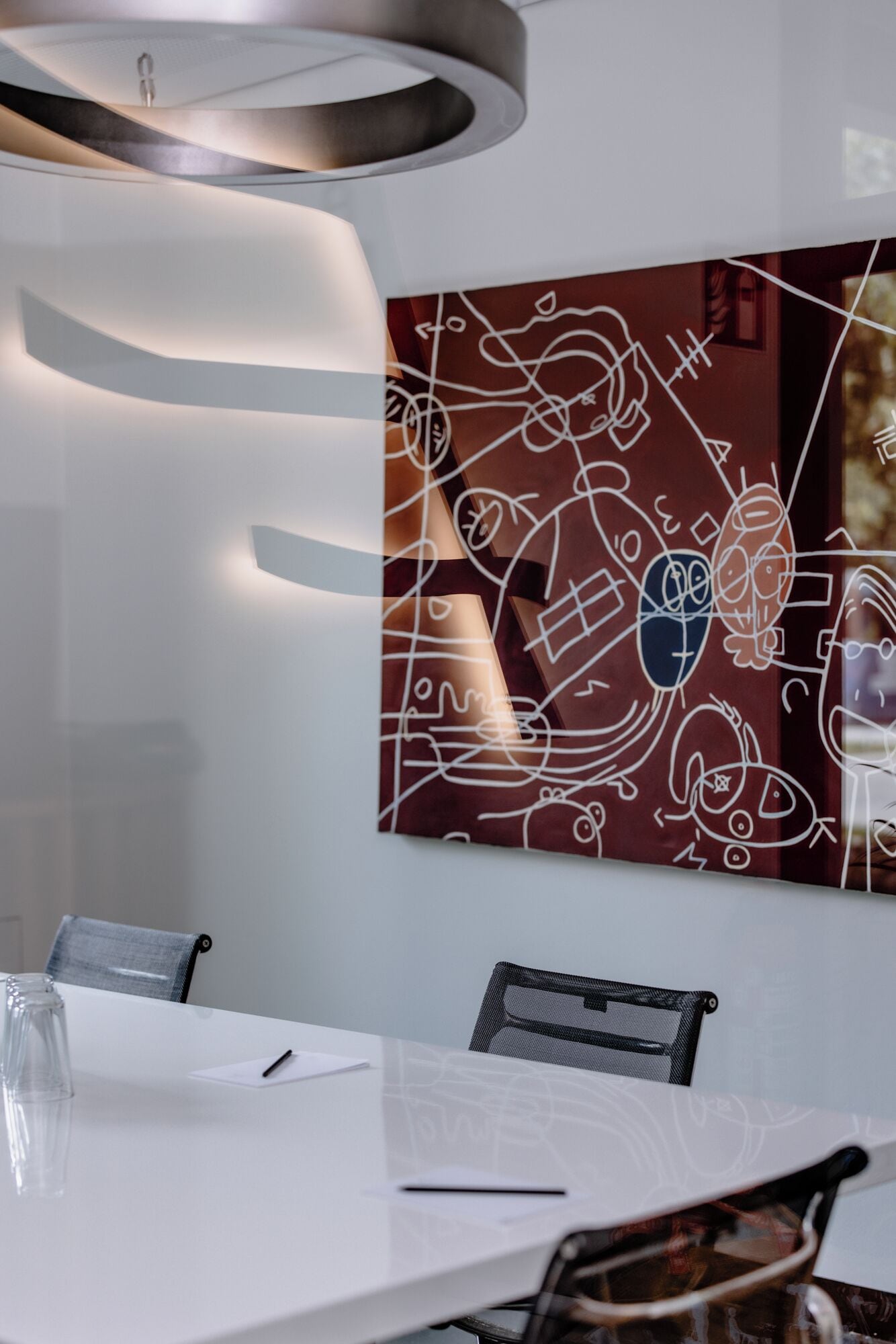 Een moderne vergaderruimte met een witte tafel, zwarte mesh-stoelen en een groot abstract kunstwerk aan de muur.