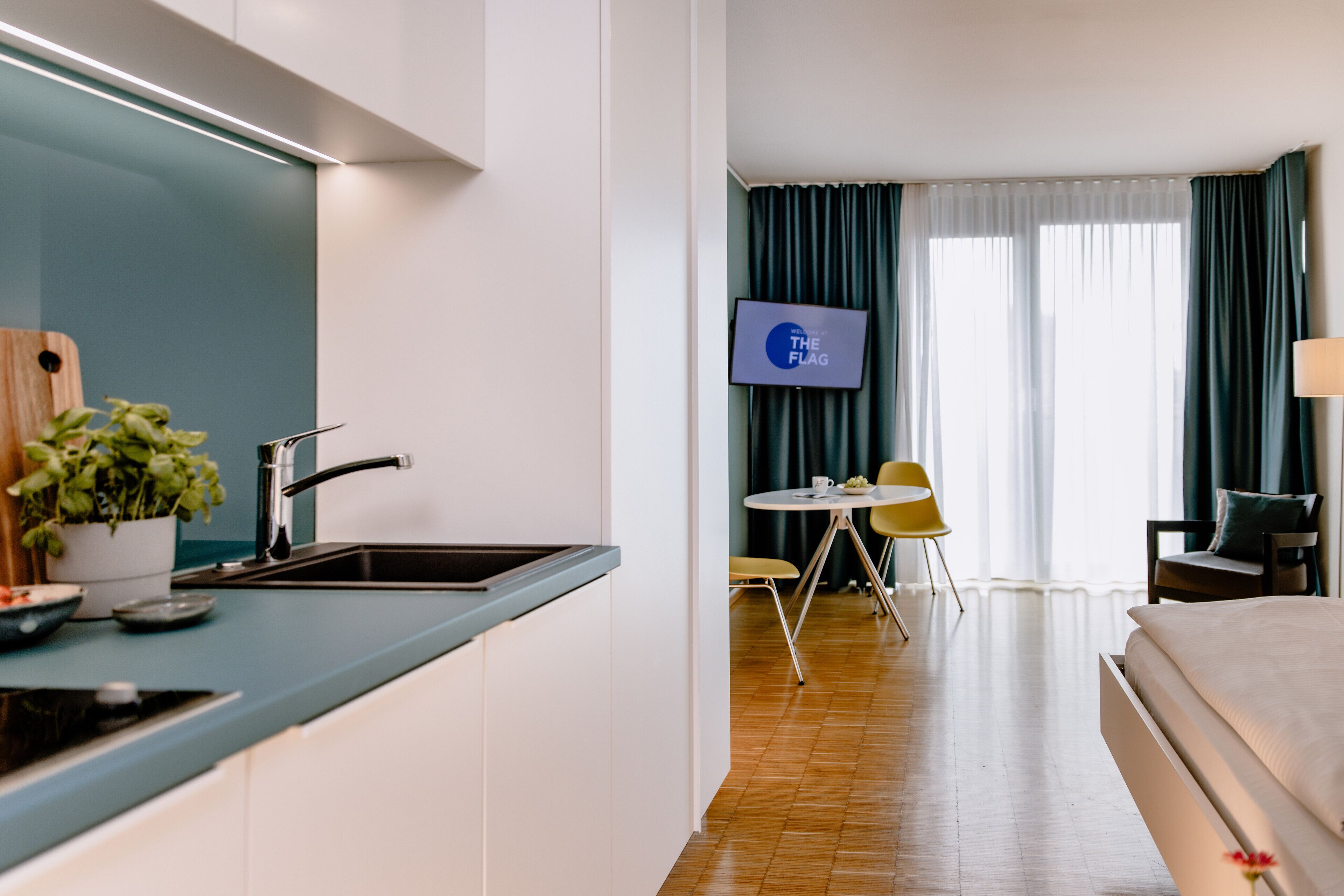 Una habitación de hotel moderna con cocina, una mesa de comedor con sillas, televisión y cama.