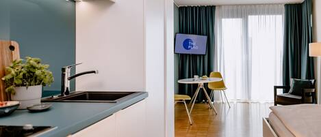 Una habitación de hotel moderna con cocina, una mesa de comedor con sillas, televisión y cama.
