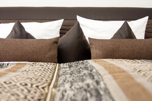 Una cama con almohadas marrones y blancas, una colcha estampada y un cabecero oscuro.