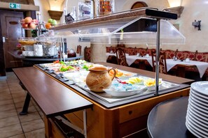 Una mesa de buffet con diversos alimentos, una jarra de leche y una estación de servicio transparente.