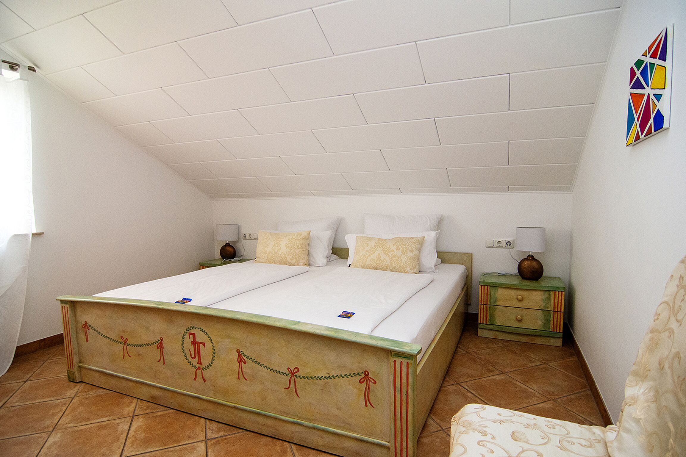 Een slaapkamer met een bed, twee nachtkastjes, een stoel en een wanddecoratie.
