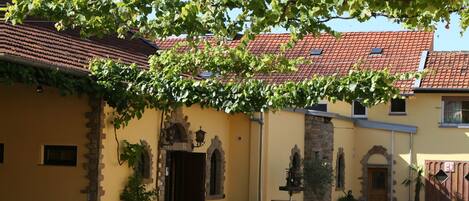 A courtyard with a building featuring a red-tiled roof, stone arches, and a yellow facade.