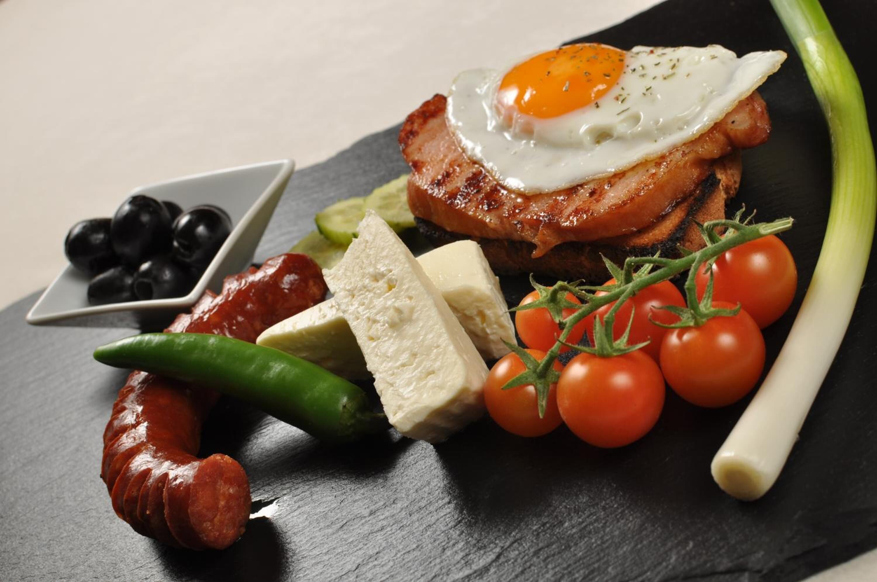 A breakfast plate with bacon, sausage, cheese, eggs, tomatoes, and olives.