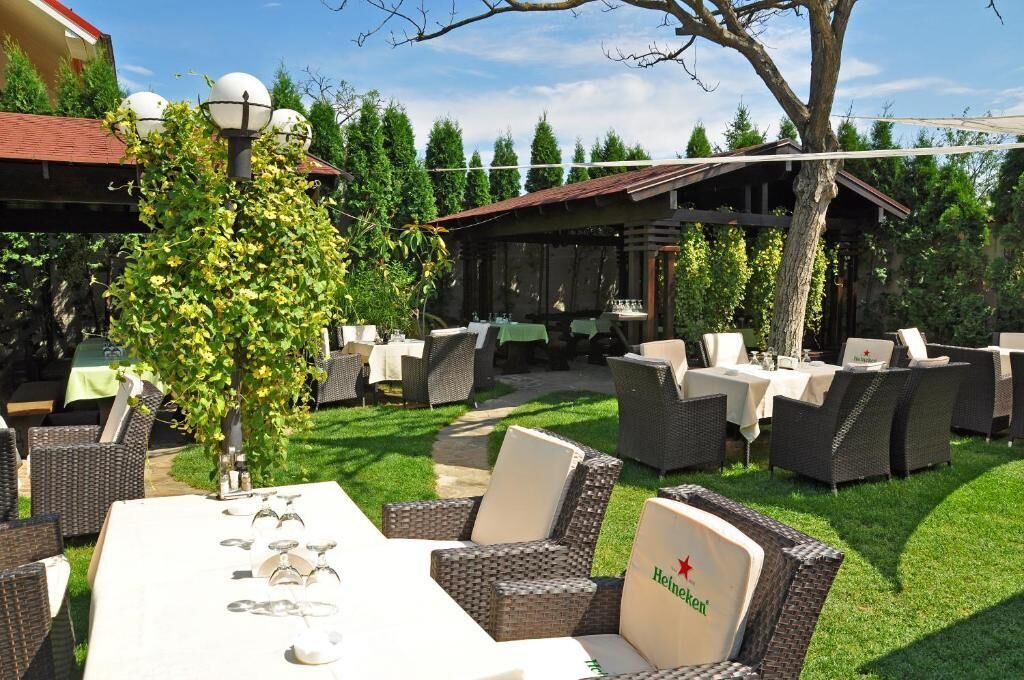 En uteservering med möbler och bord i rotting, en pergola och ett träd.