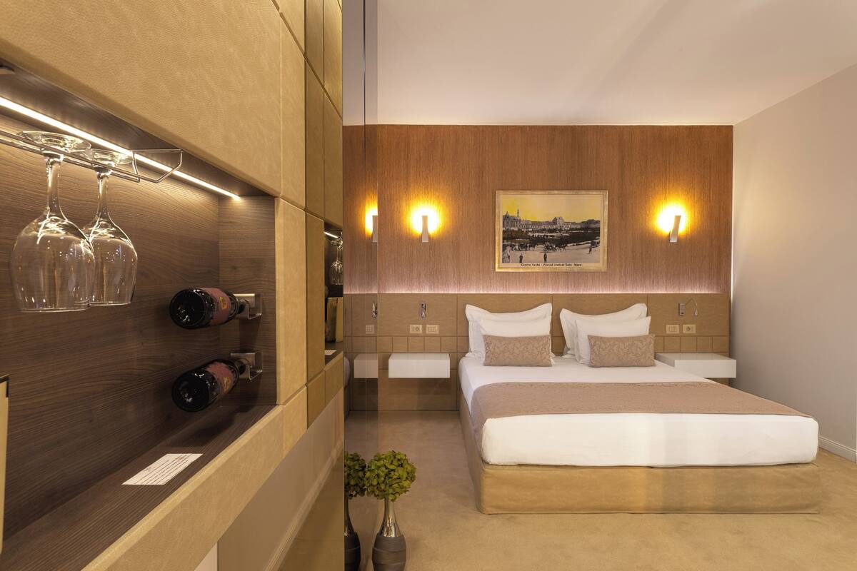 A modern hotel room with a large bed, bedside tables, a wall-mounted wine rack, and a framed picture on the wall.