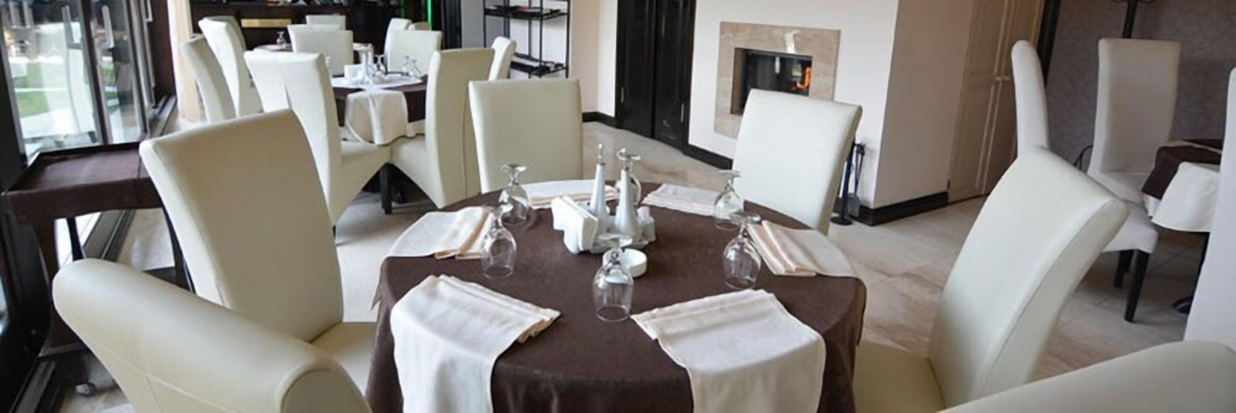 Un comedor con mesas redondas, sillas blancas y una chimenea.