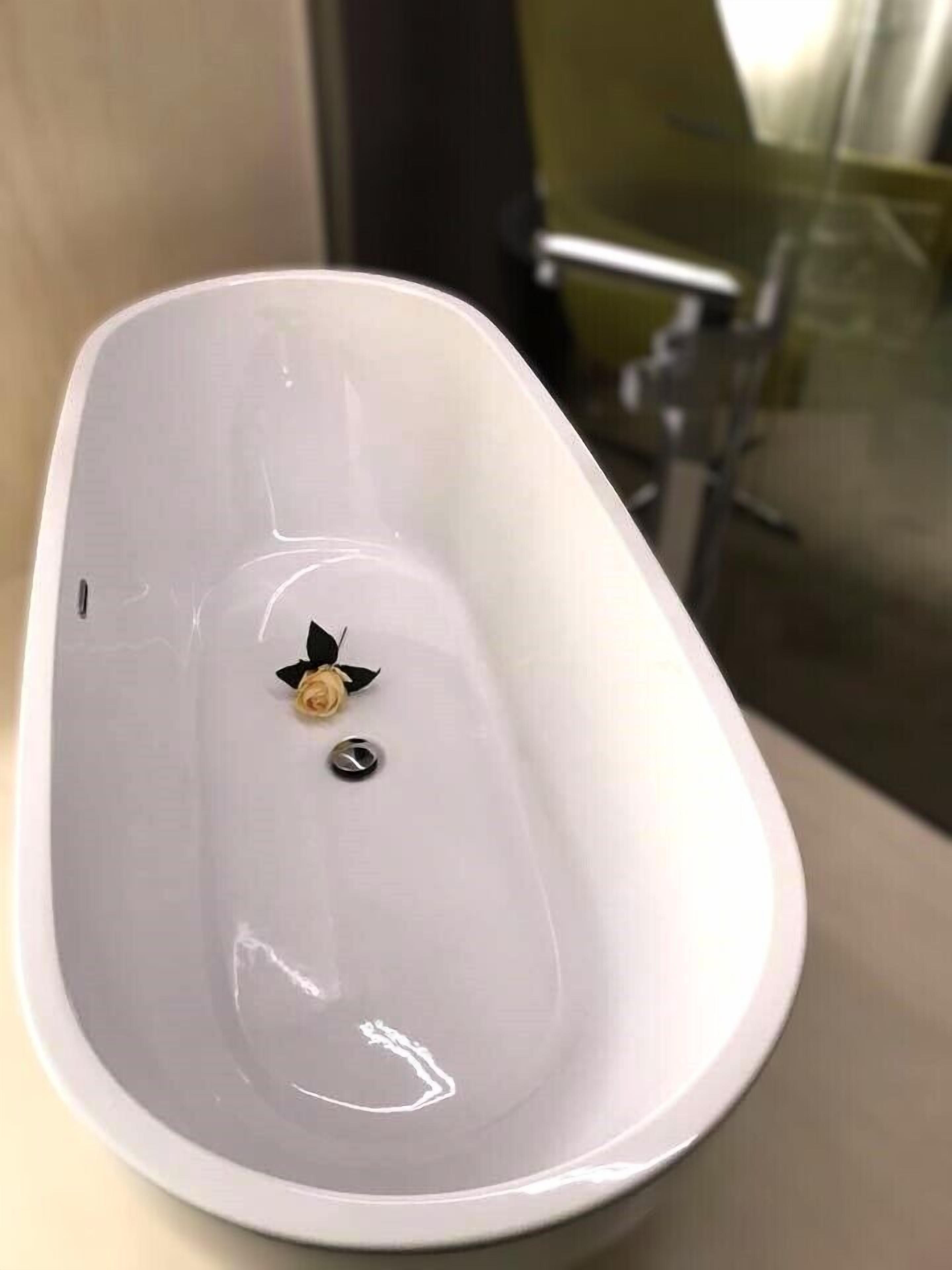 Una bañera blanca y ovalada con un solo grifo y una pequeña decoración de rosa.