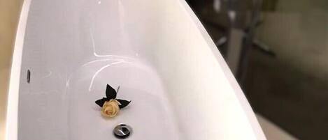Una bañera blanca y ovalada con un solo grifo y una pequeña decoración de rosa.