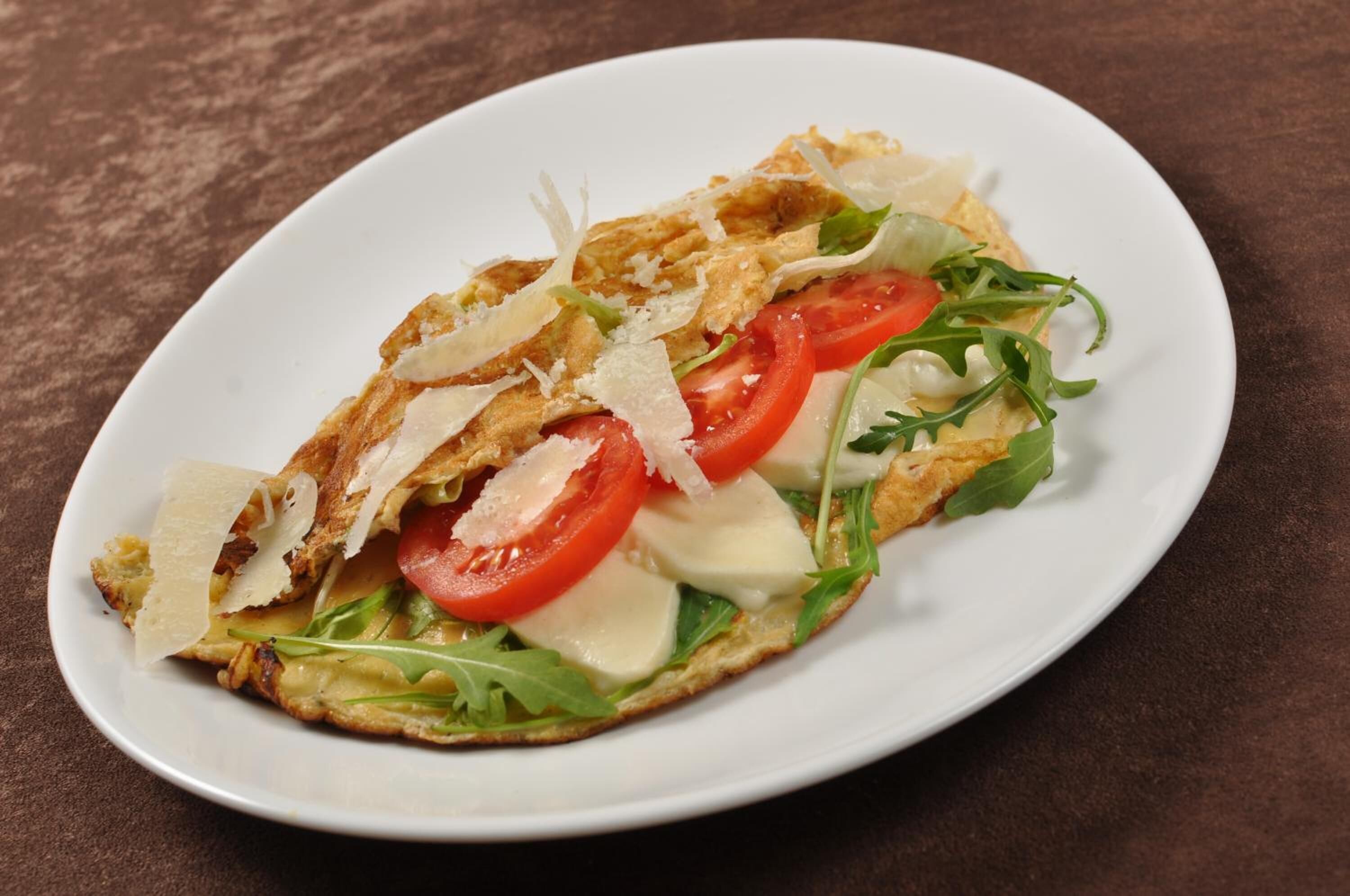 Un plato con un sándwich cubierto de queso, tomate y verduras.