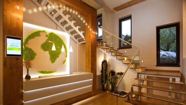 A reception area with a wooden reception desk, a staircase, and a wall with a green leaf design. - Hotel Vila Class (Satu Mare)