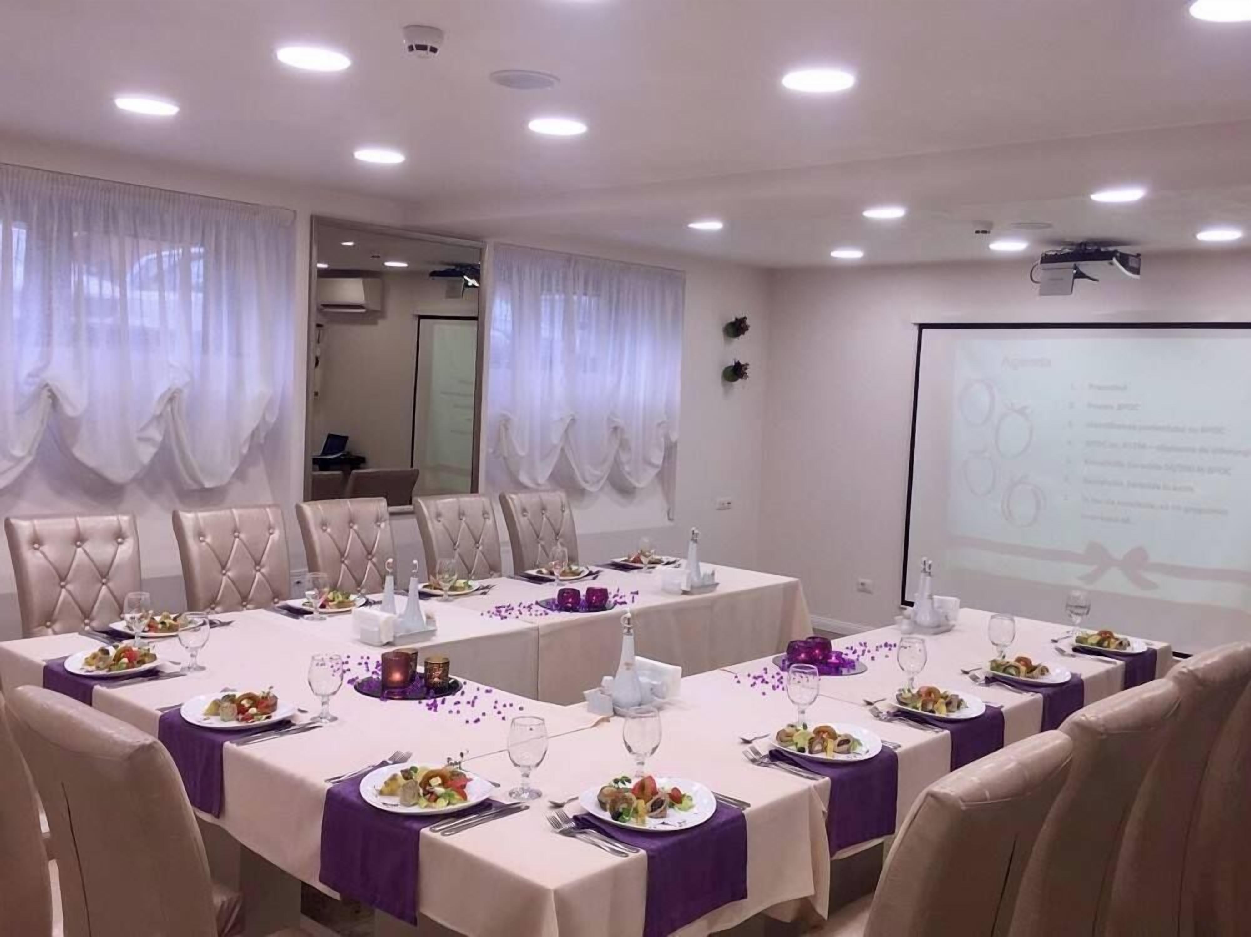 A conference room with tables set for a meal, a projector screen, and a presentation area.
