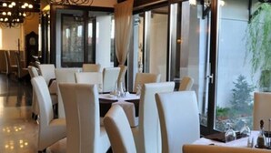 A restaurant with a modern interior, featuring white chairs and tables, large windows with a view of greenery outside. - Hotel Vila Class (Satu Mare)