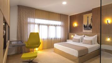 A modern hotel room with a large bed, a desk, a chair, and a large window with curtains.