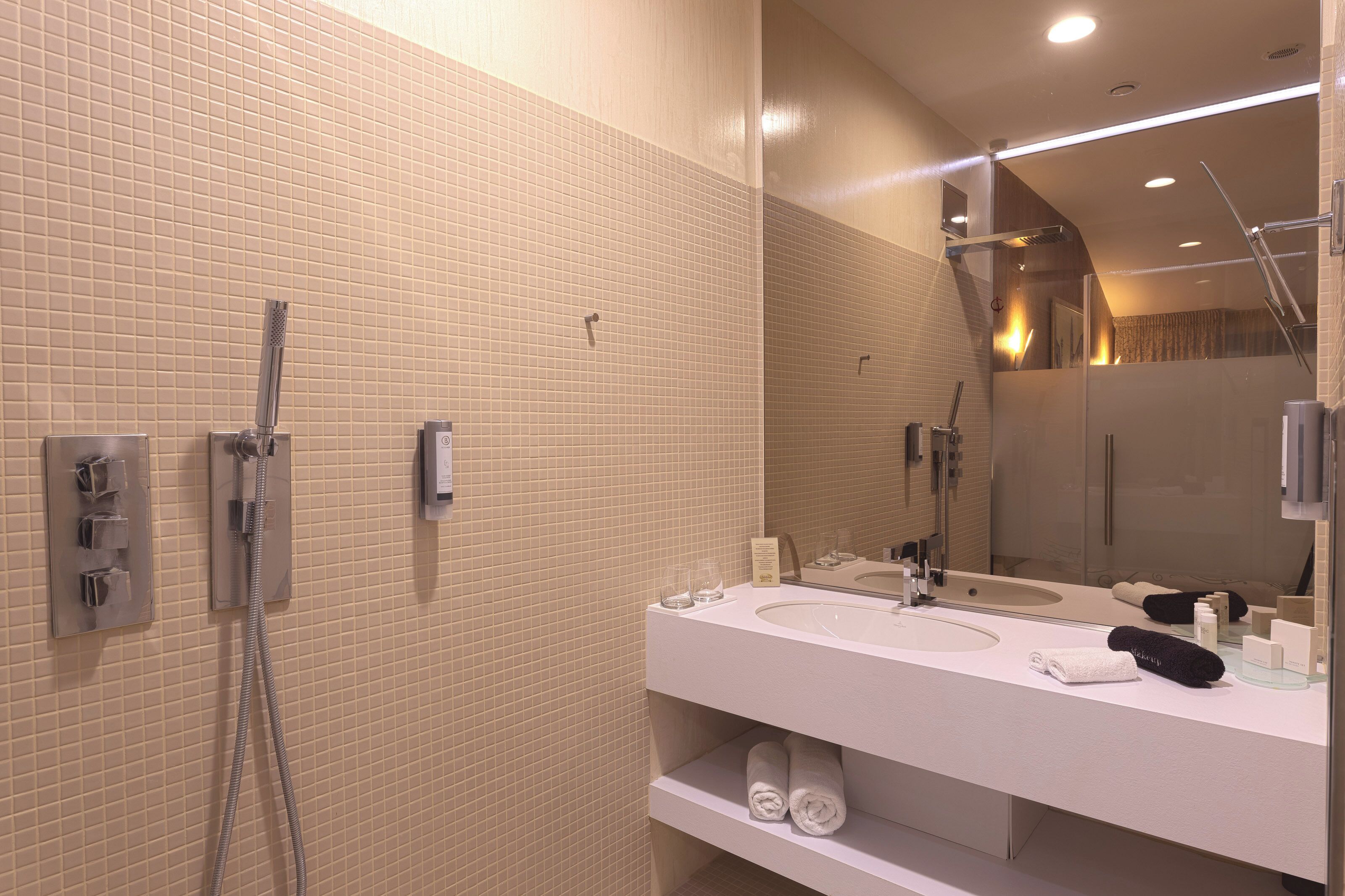A modern bathroom with beige tiled walls, a white sink, and a large mirror.