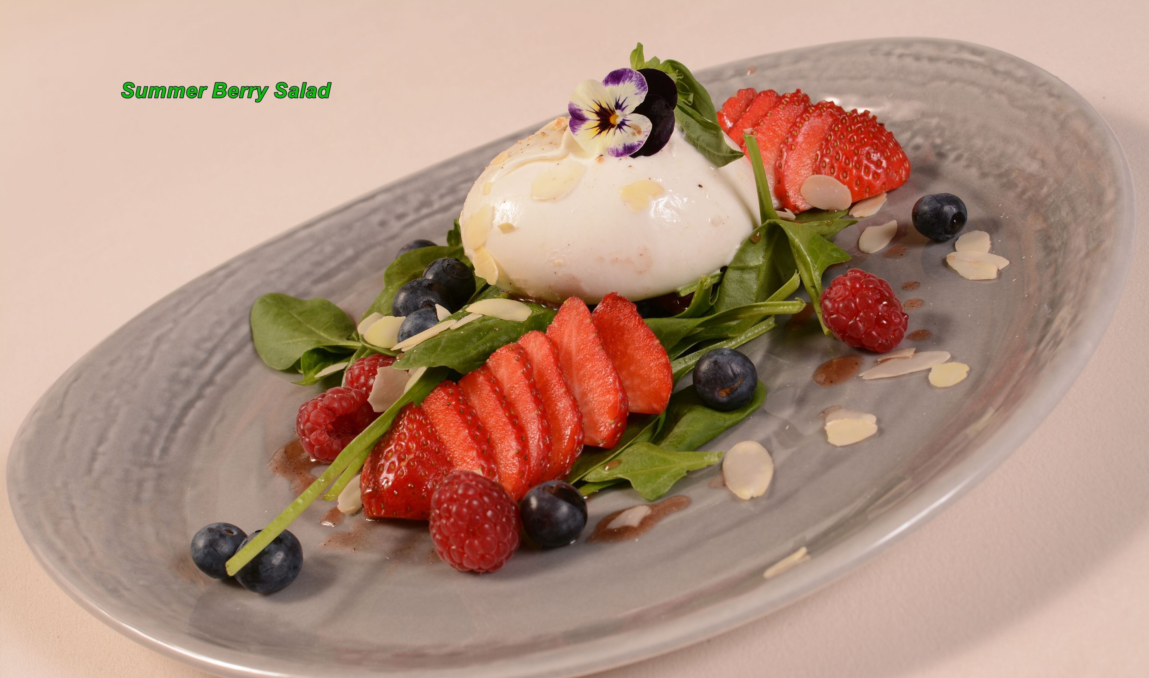 A dessert plate with a scoop of ice cream, strawberries, blueberries, raspberries, and almonds.