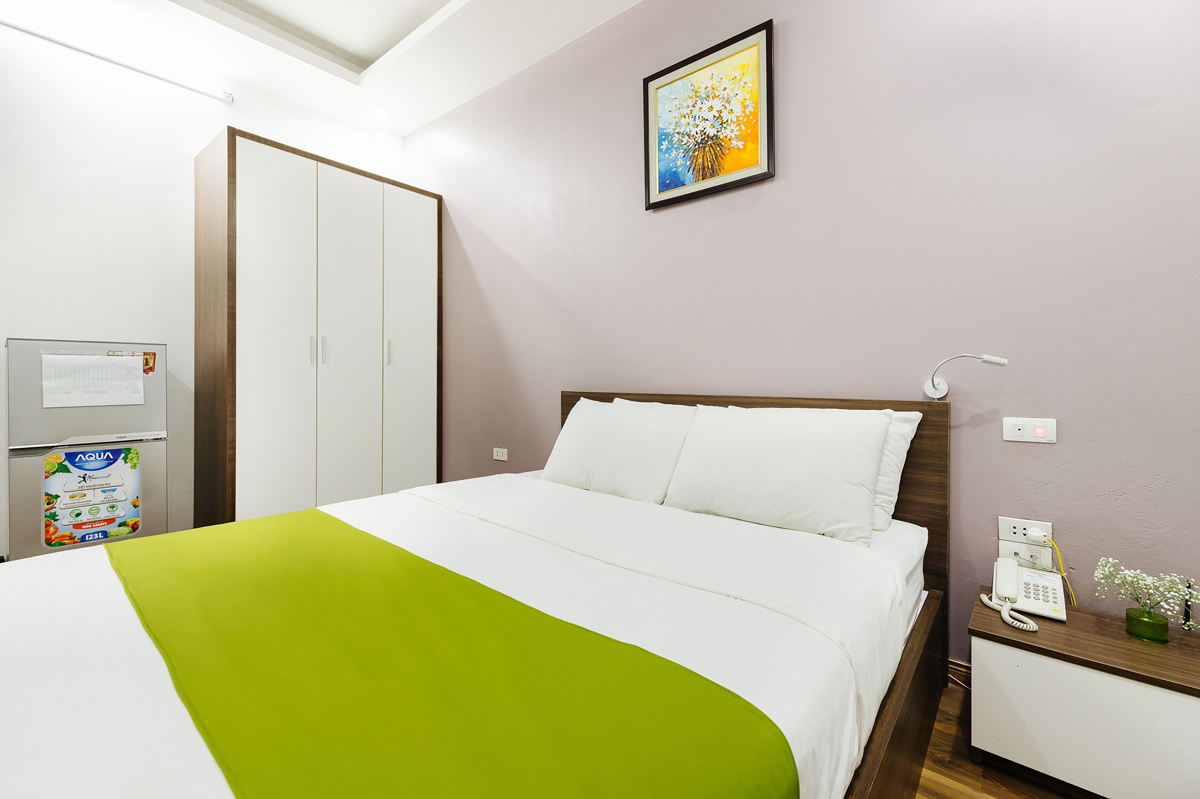 Una habitación de hotel con una cama, una mesita de noche con un teléfono, un cuadro colgado en la pared y un minibar.