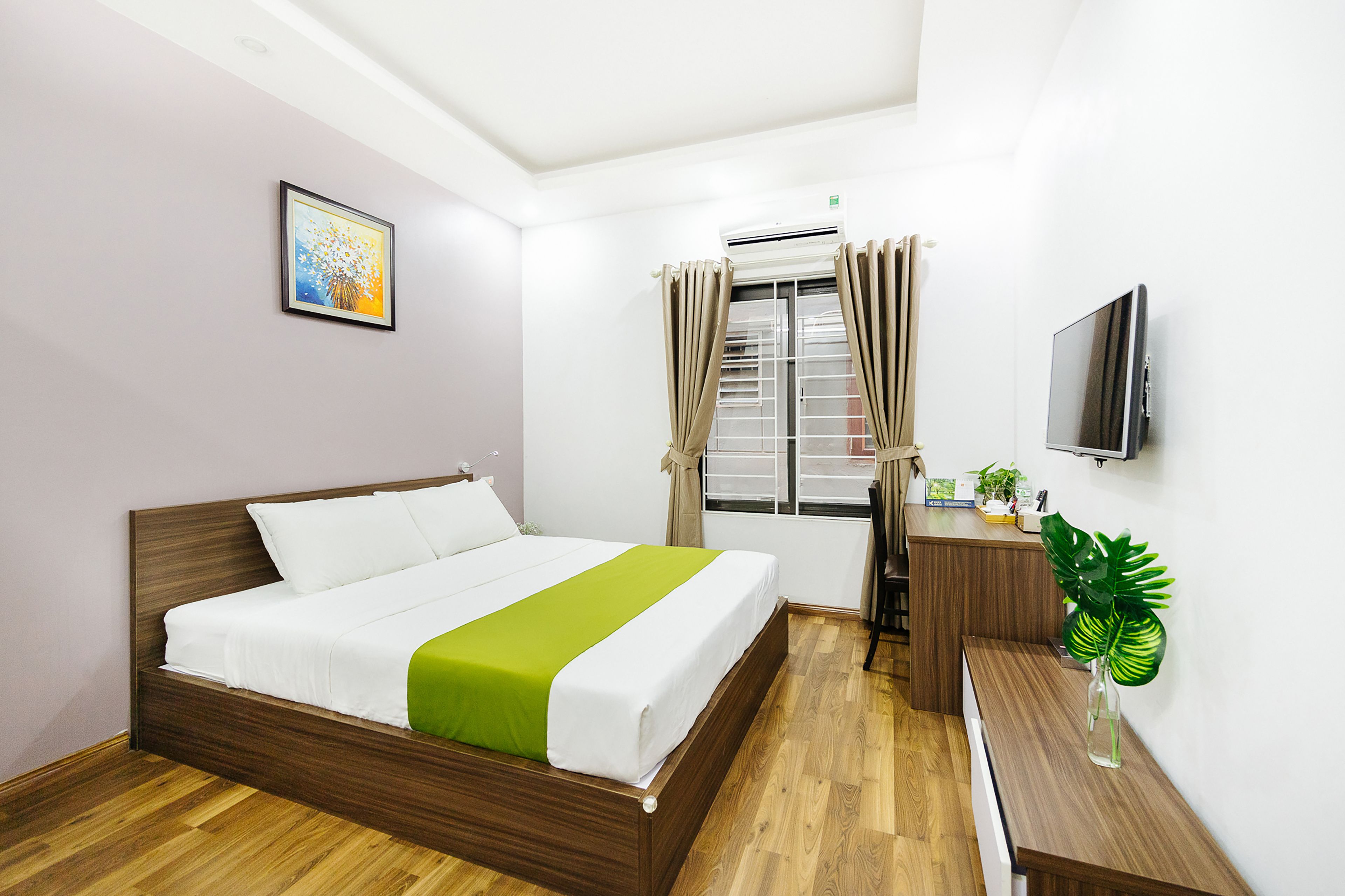 A hotel room with a wooden bed, a desk with a chair, a television, and a window with curtains.