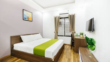 A hotel room with a wooden bed, a desk with a chair, a television, and a window with curtains.