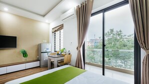 Una habitación de hotel con cama, escritorio, televisor y un ventanal con cortinas.