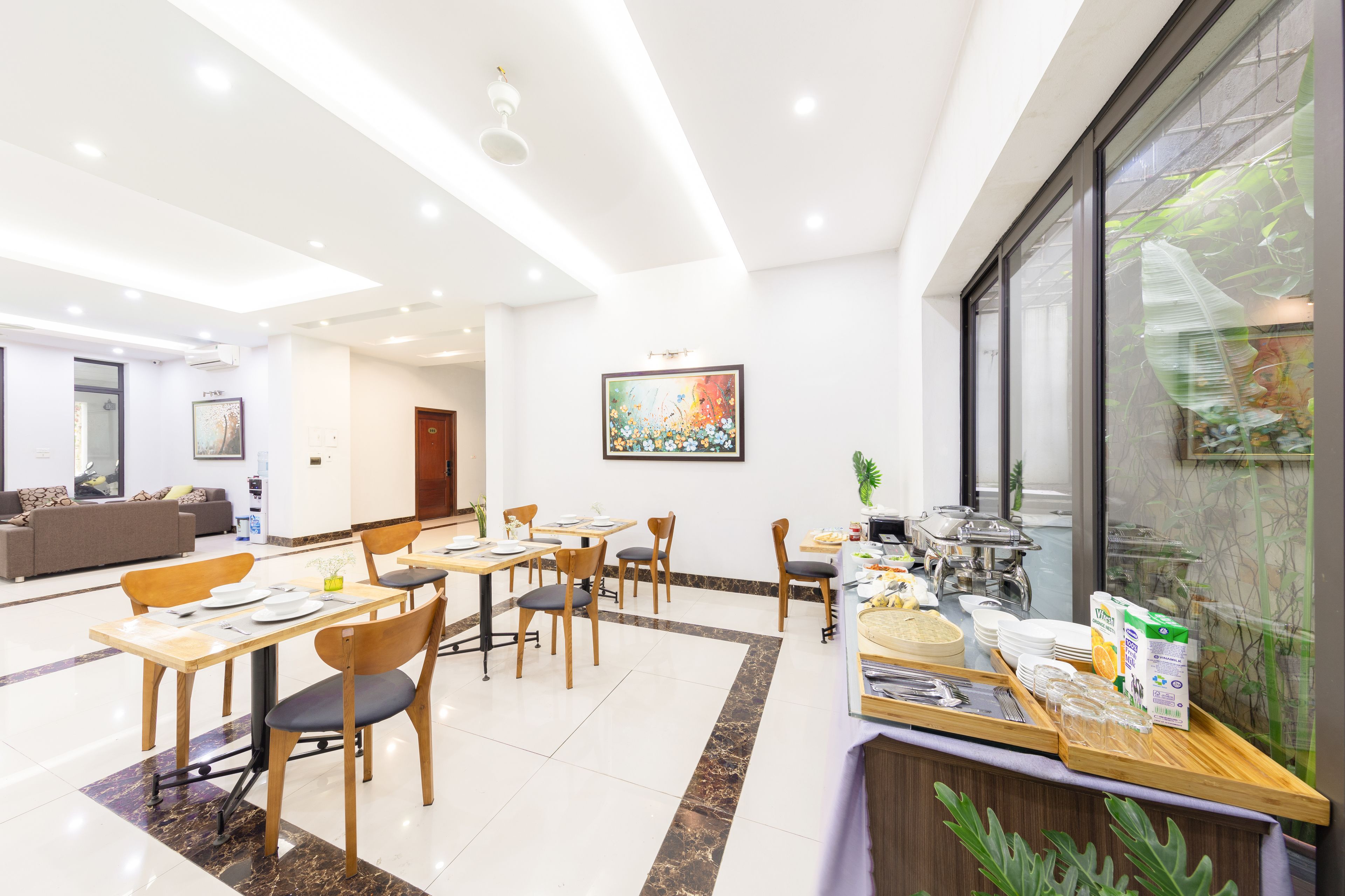 Un'area pranzo moderna con tavoli e sedie, un banco per il buffet e un'ampia finestra con vista su un giardino.