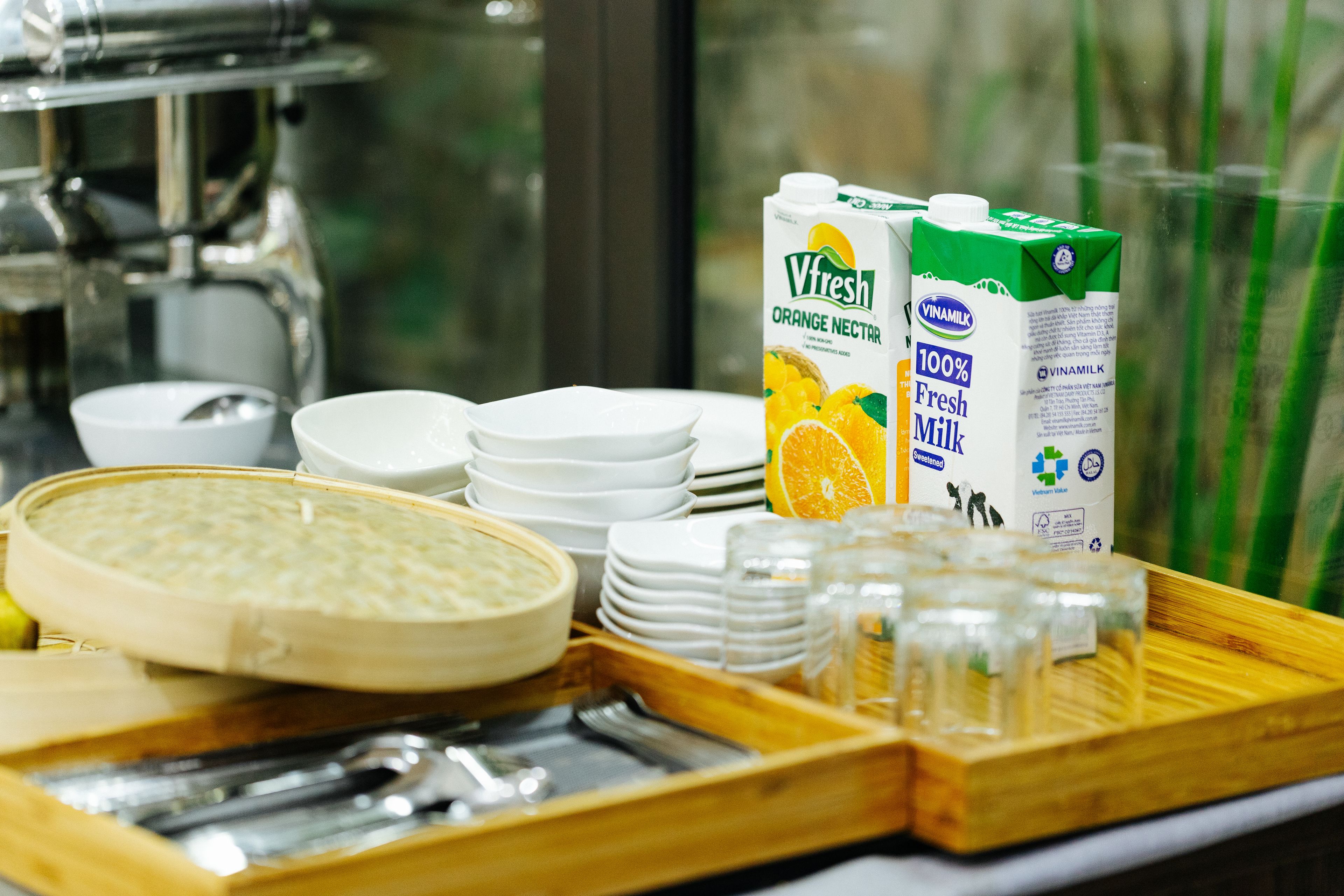 A breakfast buffet setup with orange juice cartons, bowls, plates, and utensils.