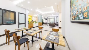 Un comedor de hotel moderno con mesas dispuestas para cuatro personas, una recepción y un cuadro grande con motivos florales en la pared.