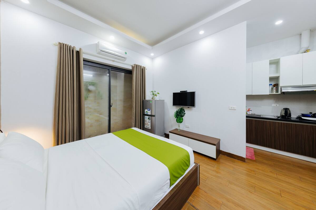 A hotel room with a bed, a kitchenette, a TV, and an air conditioning unit.