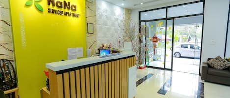 A reception desk with a yellow wall and a sign that reads "HaNa Serviced Apartment".