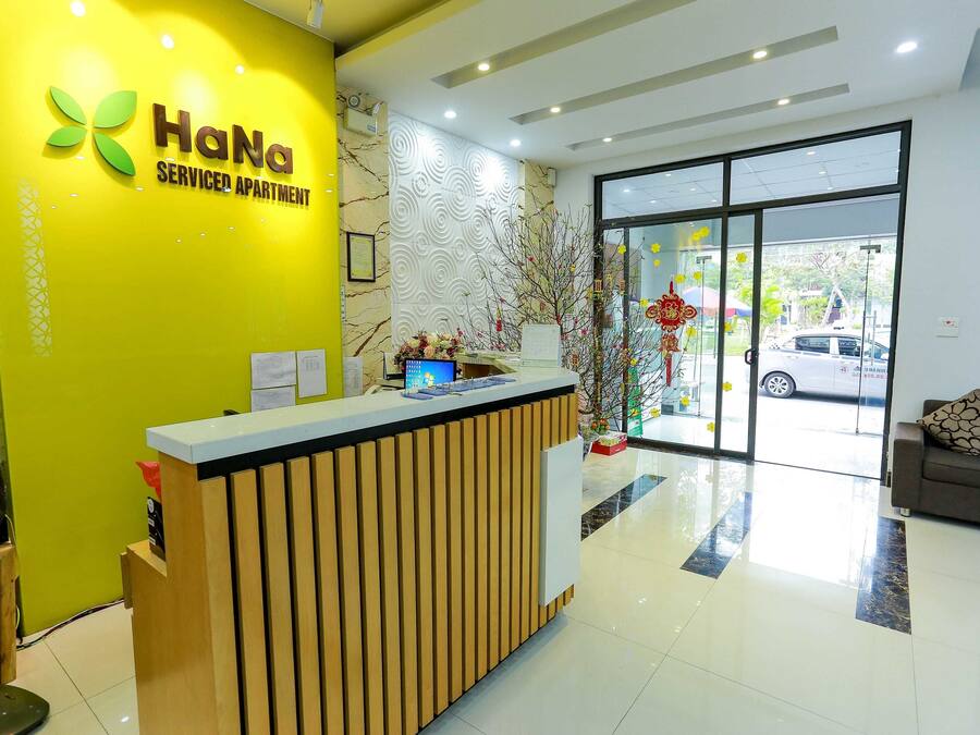 A reception desk with a yellow wall and a sign that reads "HaNa Serviced Apartment".