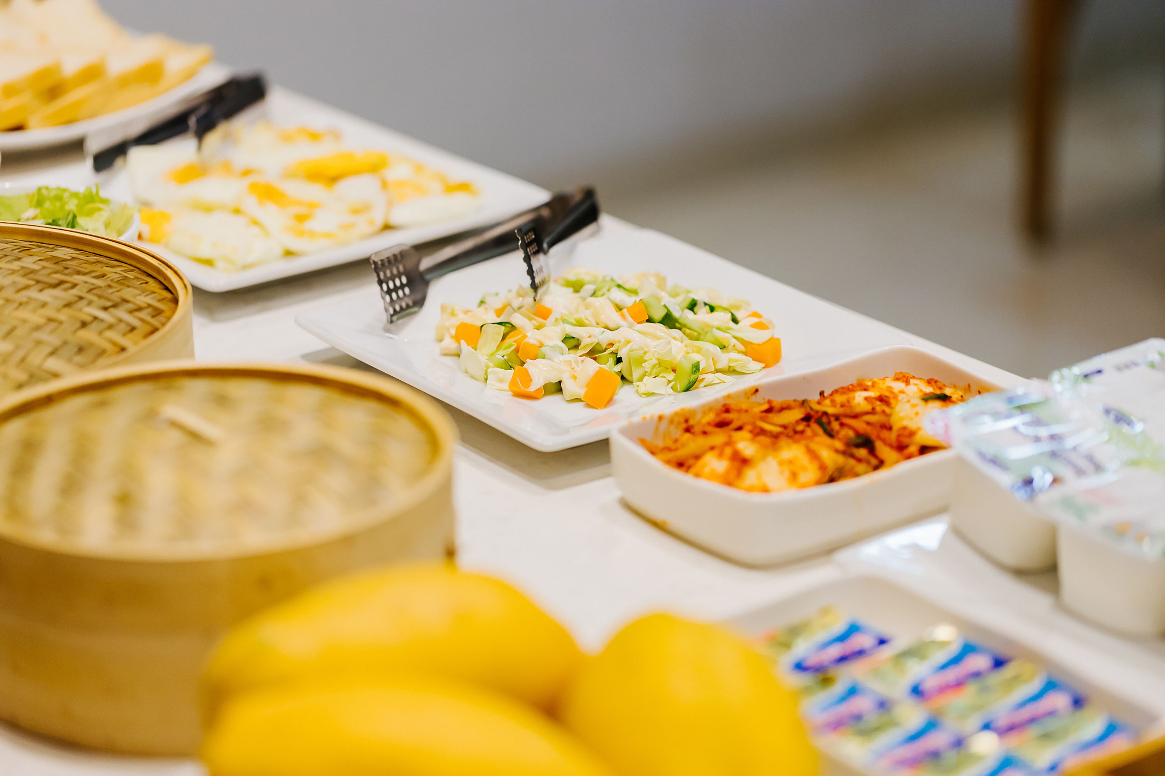 A buffet table with various dishes, including a bowl of soup, a plate of salad, and several containers of dips.