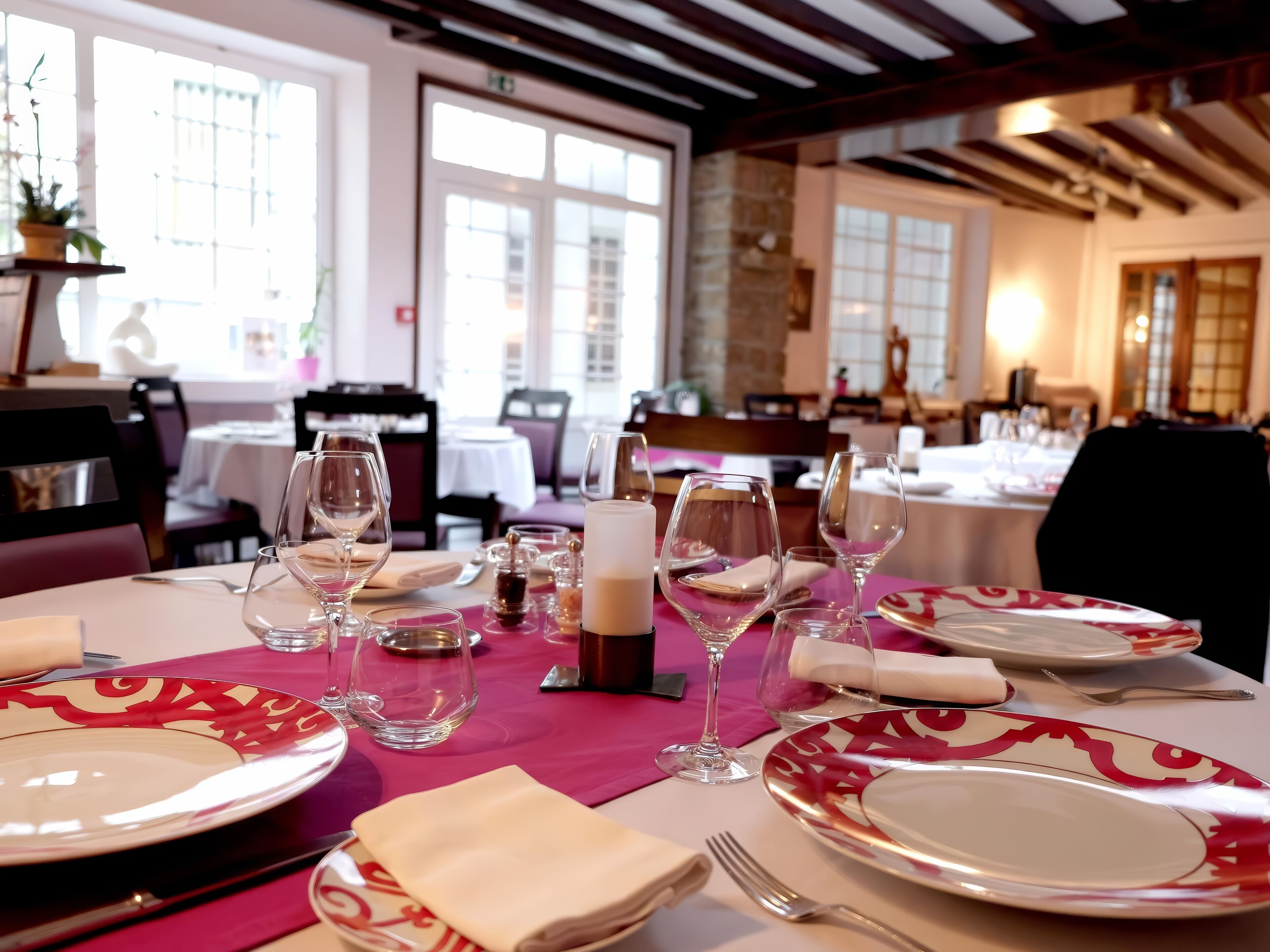 A dining table set with plates, glasses, and cutlery, with a pink tablecloth and a candle centerpiece.